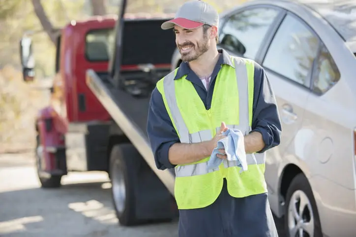 Carolina Collision and Frame Service | A flatbed truck driver smiling wearing a yellow safety vest after hitching a car to his truck