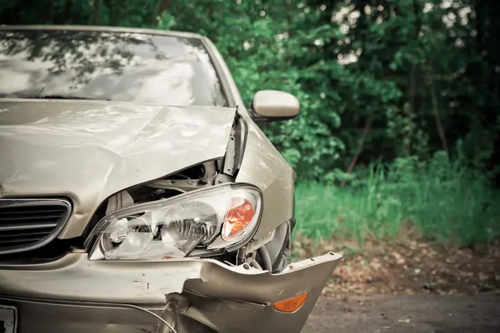 Carolina Collision and Frame Service | Beige car with body damage parked near a wooded lot